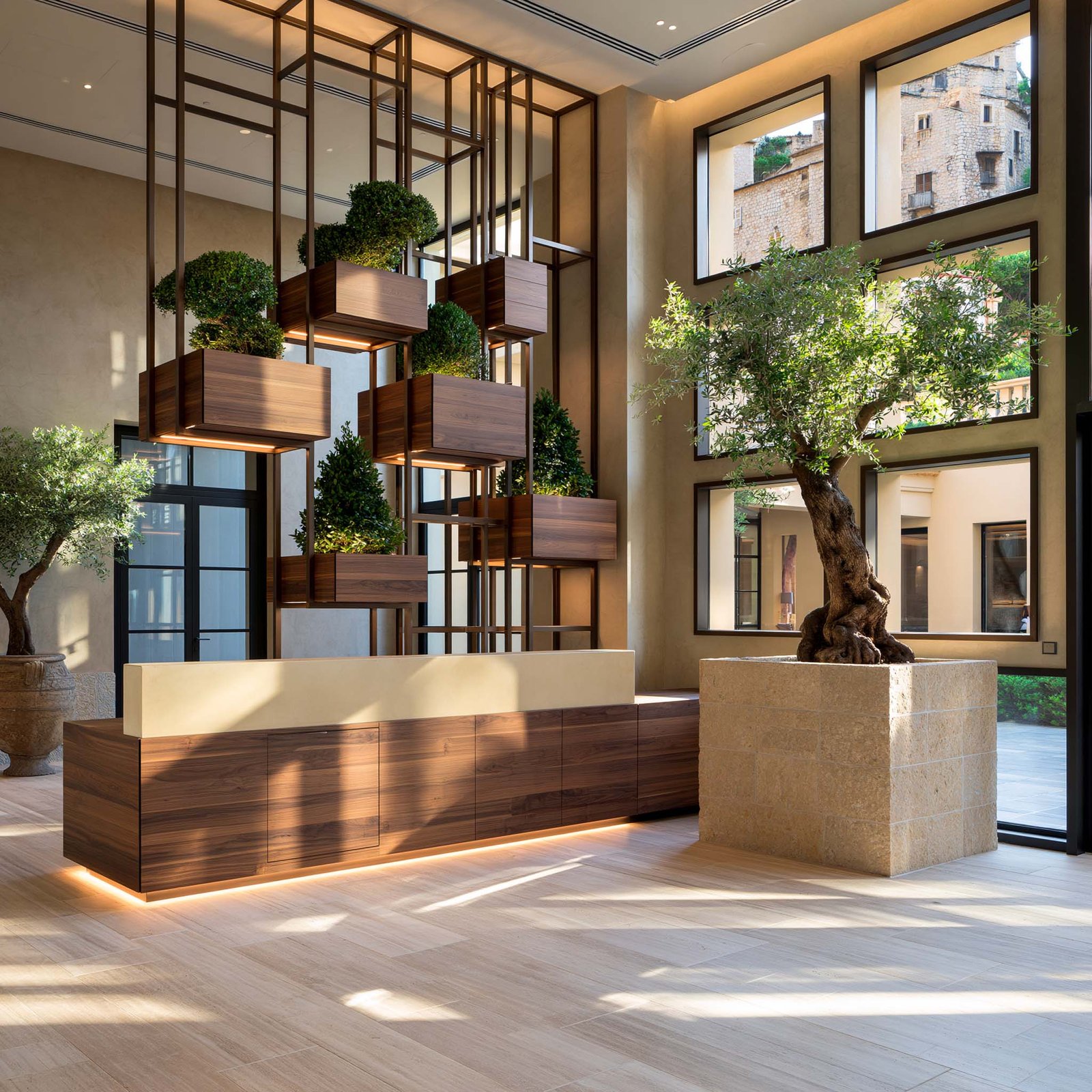 Hospitalité à Monaco — lobby d’hôtel boutique avec partition botanique en acier noirci et noyer fumé portant des masses de Buxus sempervirens et Laurus nobilis en strates, comptoir noyer fumé et olivier en bac monolithique.