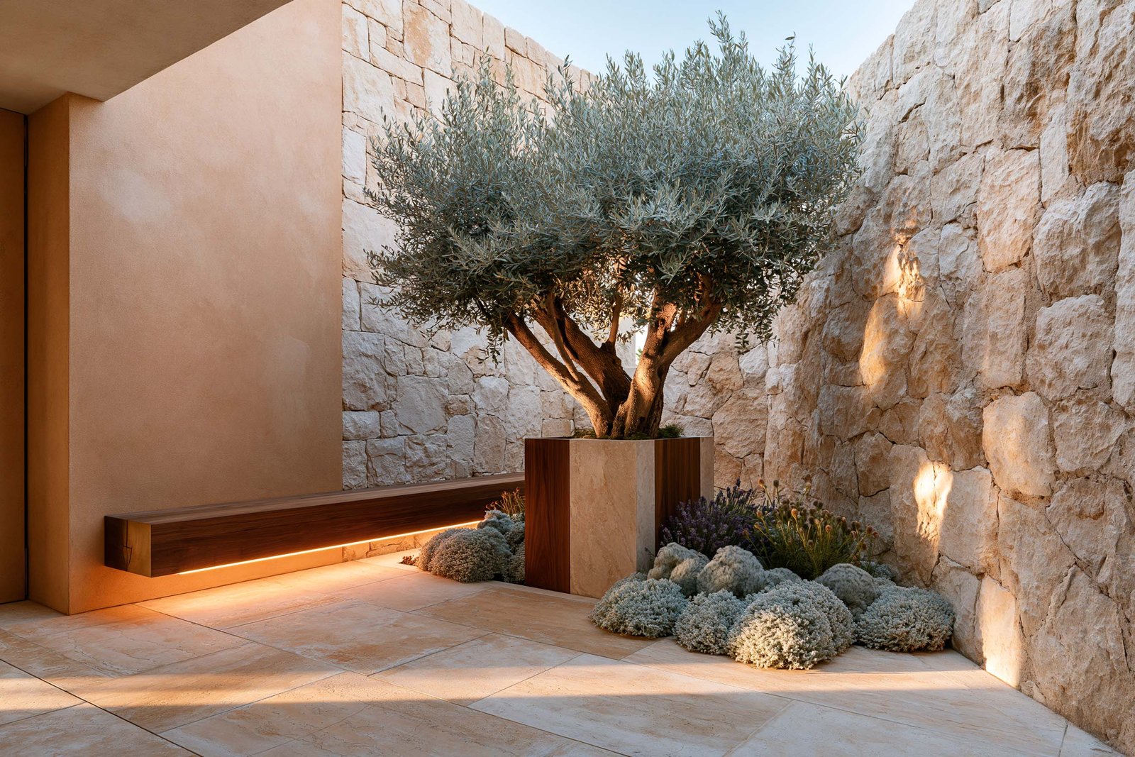 Patio méditerranéen — cour intérieure d’une villa à Èze en fin d’après-midi, banc Lignum™ Block en noyer fumé adossé à un mur en pierre brute calcaire claire, Olea europaea en port libre méditerranéen au centre du patio dans un planter Lignum™ Petra à âme travertin clair, Lavandula angustifolia et Helichrysum italicum en masses au pied, sol en grandes dalles de travertin clair warm honey, golden hour chaud, Paracelsus Gardens™